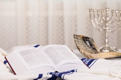 Photo of Open Torah book, Tallit and Shofar on table indoors. Rosh Hashanah holiday attributes