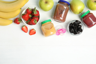 Photo of Jars with baby food and fresh ingredients on white wooden table, flat lay. Space for text