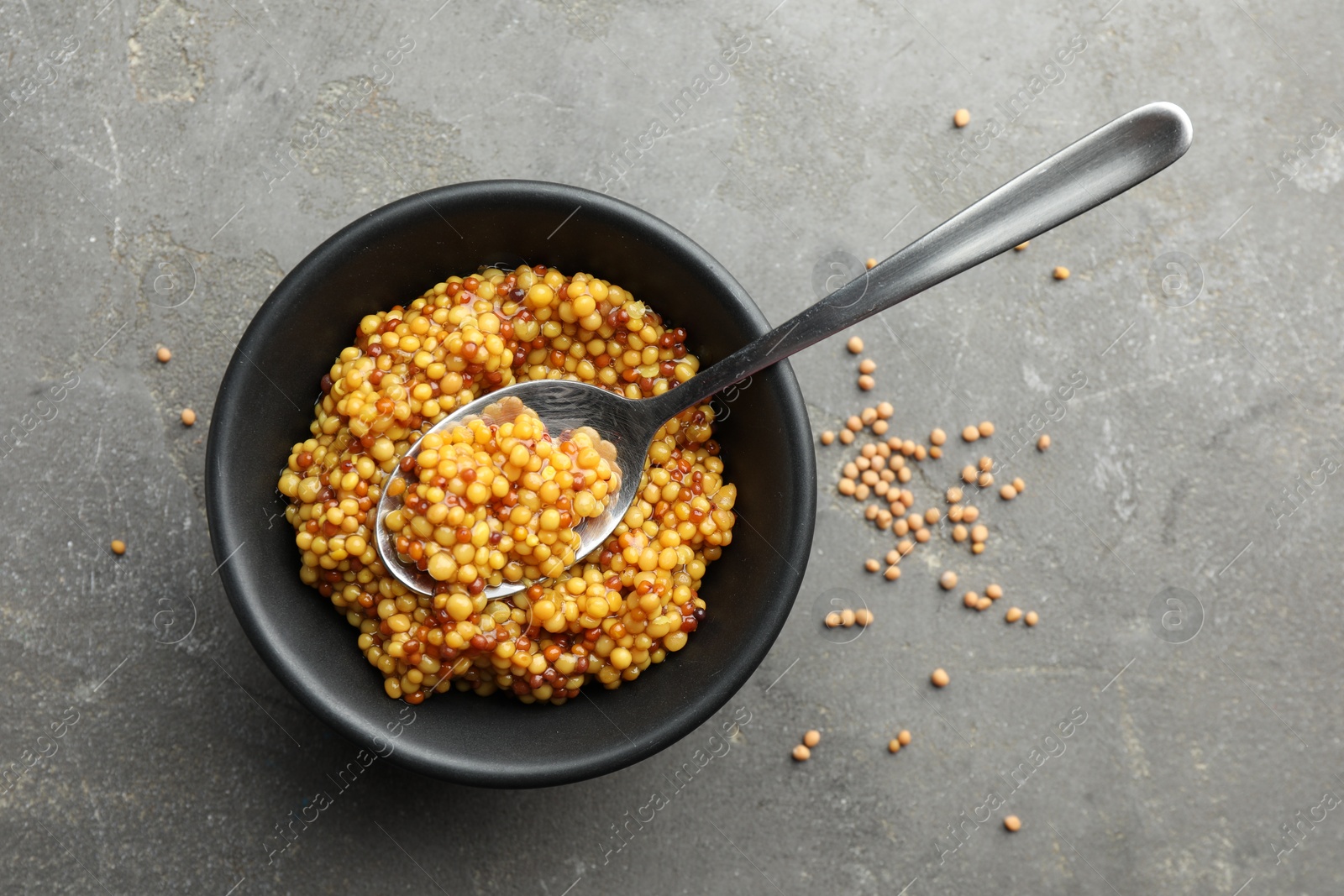 Photo of Whole grain mustard in bowl, spoon and dry seeds on grey table, flat lay. Space for text