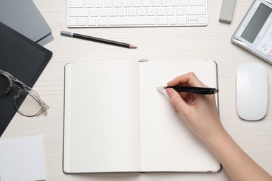 Photo of Woman writing in notebook at white wooden table, top view