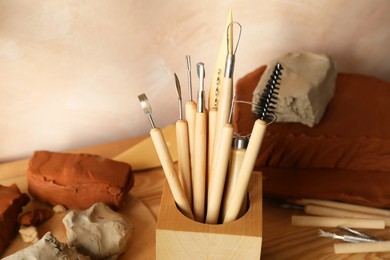 Photo of Clay and set of modeling tools on wooden table in workshop, closeup