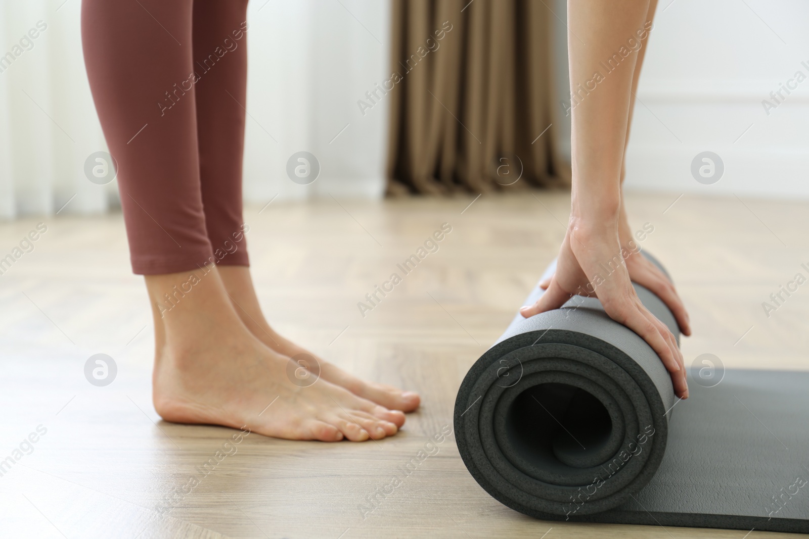 Photo of Woman rolling grey yoga mat indoors, closeup