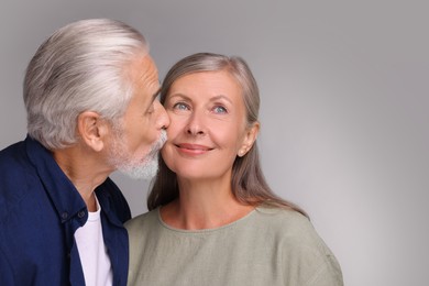 Senior man kissing his beloved woman on light grey background, space for text