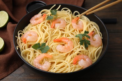 Tasty spaghetti with shrimps and parsley in bowl on wooden table, closeup