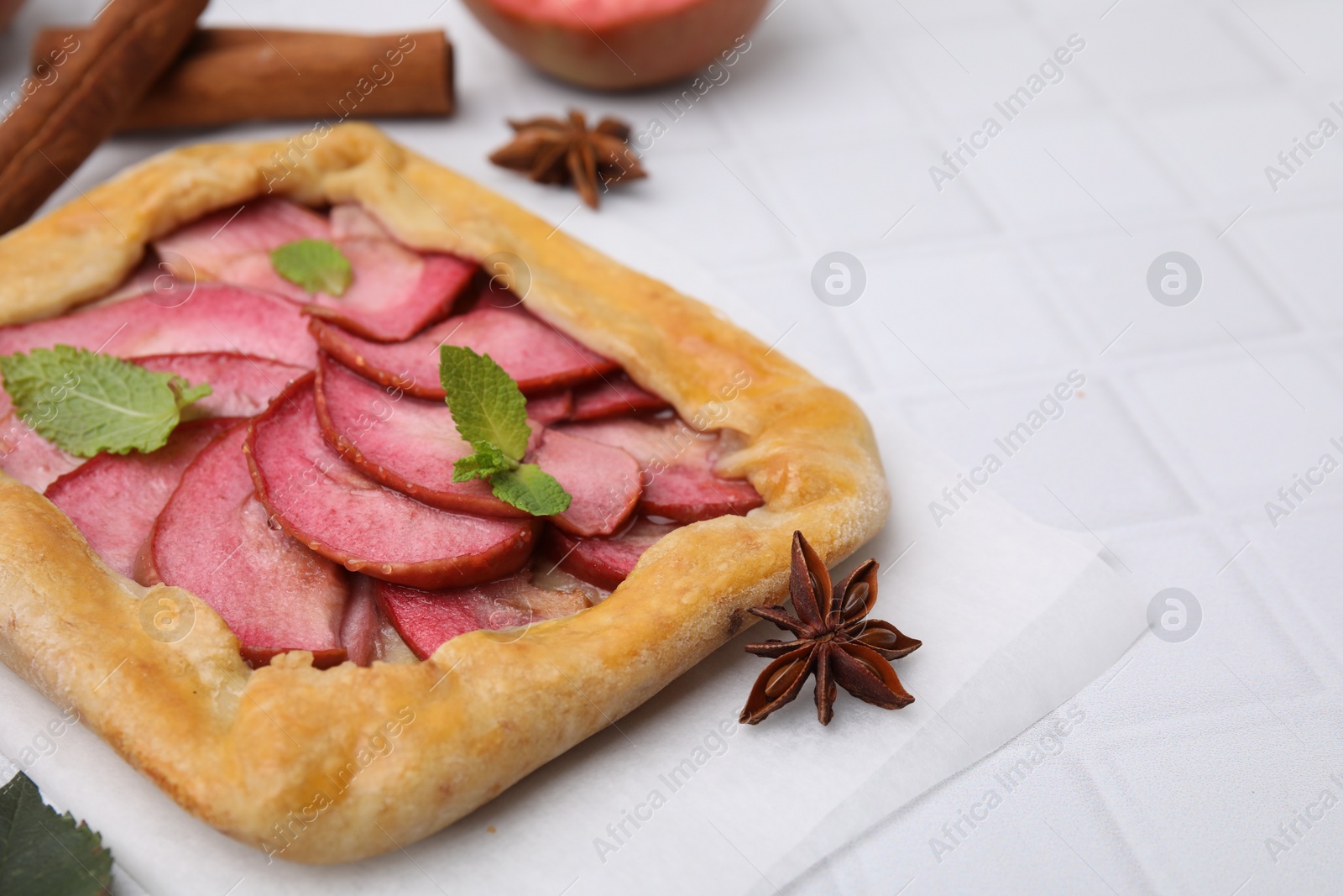 Photo of Delicious apple galette with mint on white tiled table, closeup. Space for text