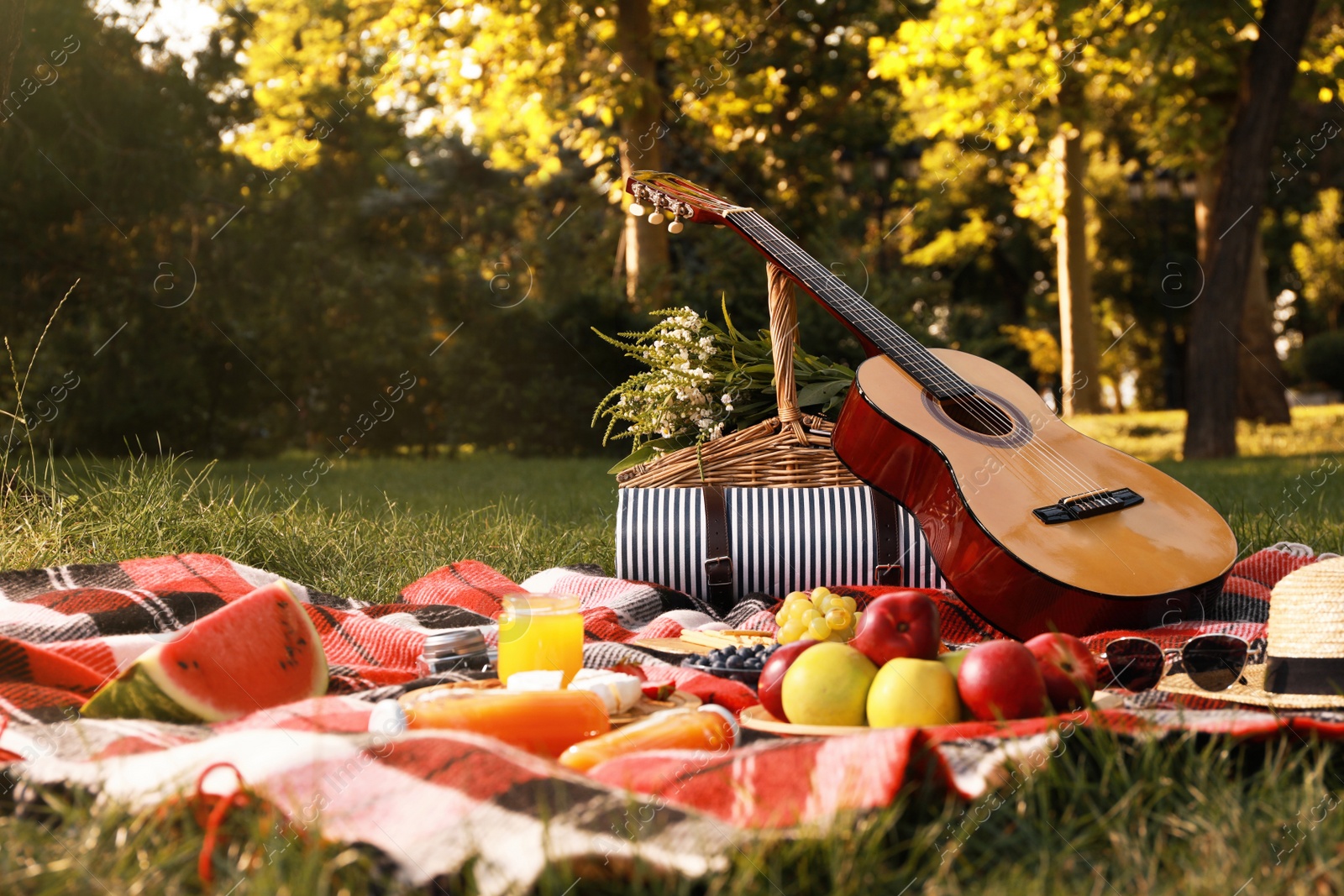 Photo of Picnic basket, guitar, food and drinks on plaid in summer park