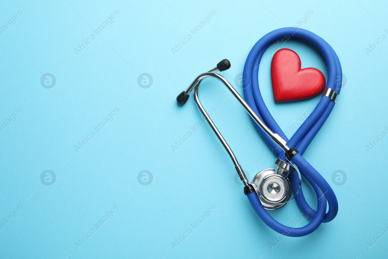 Photo of Stethoscope and red heart on light blue background, top view. Space for text