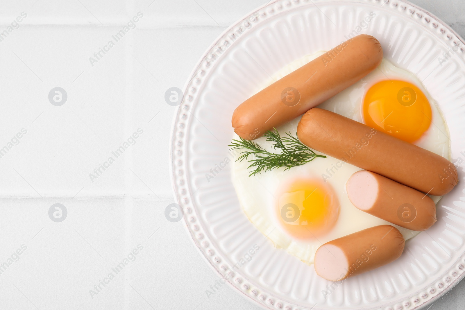Photo of Delicious boiled sausages, fried eggs and dill on white tiled table, top view. Space for text