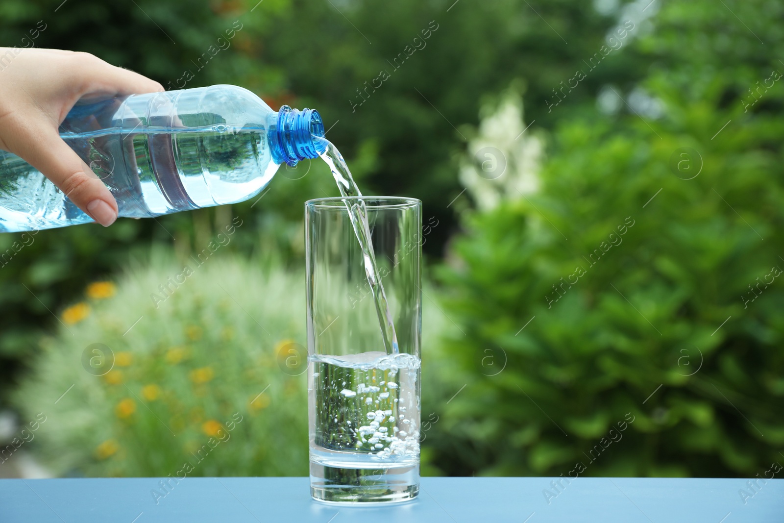 Photo of Woman pouring water from bottle into glass on table outdoors, closeup