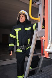 Firefighter in uniform and helmet near fire truck at station