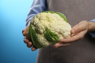 Woman holding fresh cauliflower against blue background, closeup