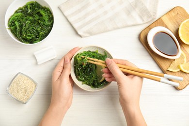 Photo of Woman eating Japanese seaweed salad at white wooden table, top view