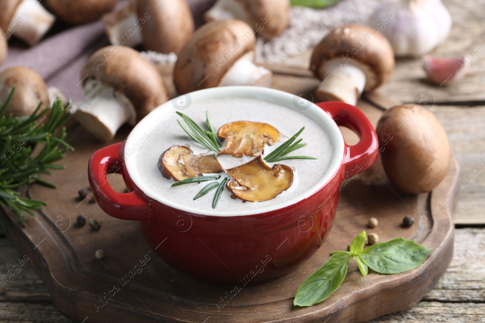 Photo of Delicious homemade mushroom soup in ceramic pot and fresh ingredients on wooden table