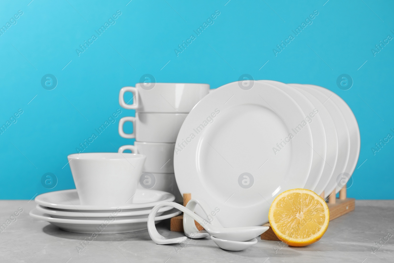 Photo of Clean tableware and half of lemon on grey table against light blue background