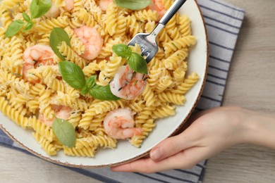 Photo of Woman eating delicious pasta with shrimps, basil and parmesan cheese at table, top view