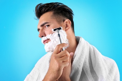 Handsome young man shaving on color background