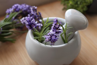 Photo of Mortar with fresh lavender flowers, rosemary and pestle on wooden table, closeup