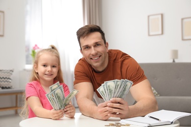 Father and daughter counting money at table indoors