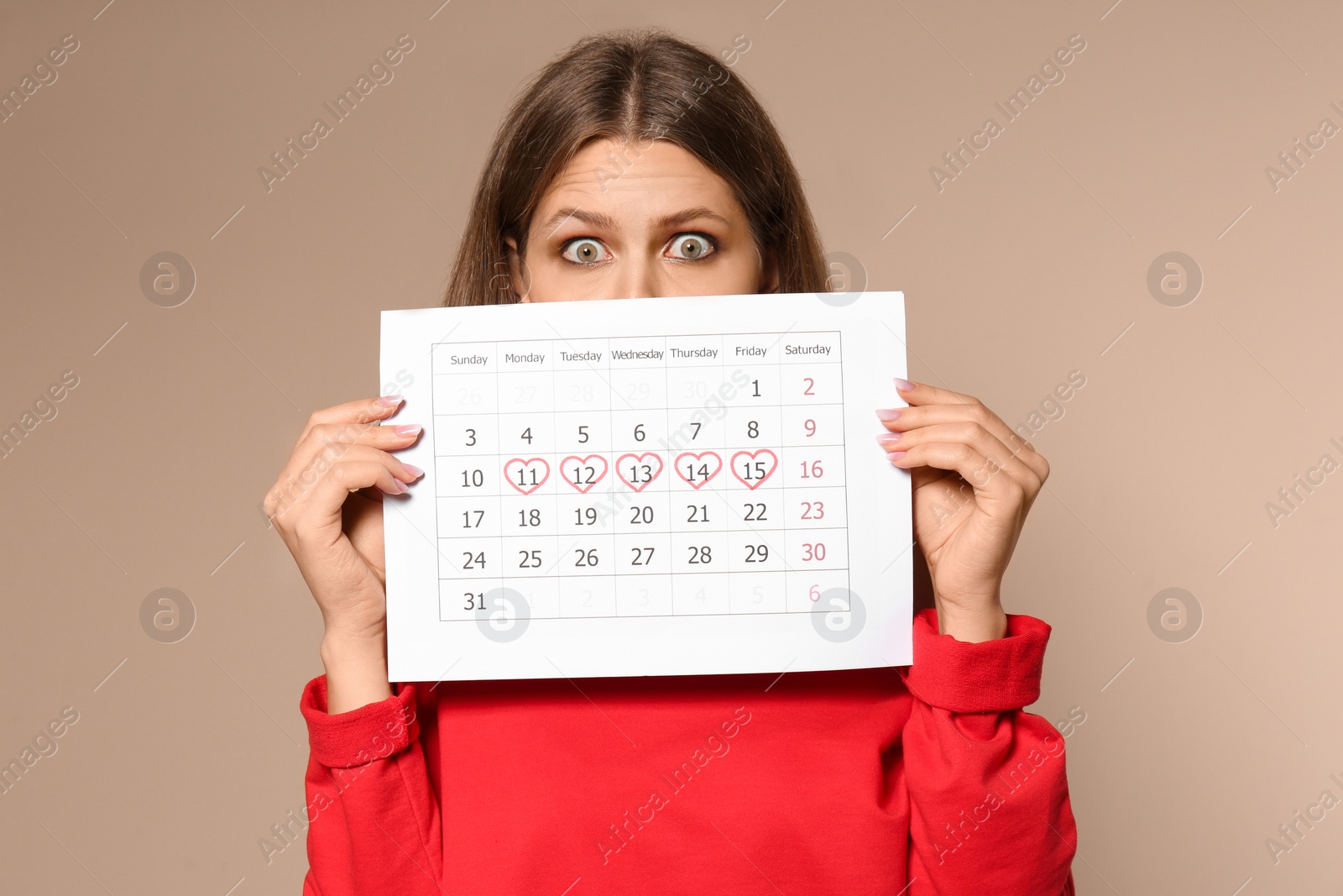 Photo of Young woman holding calendar with marked menstrual cycle days on beige background