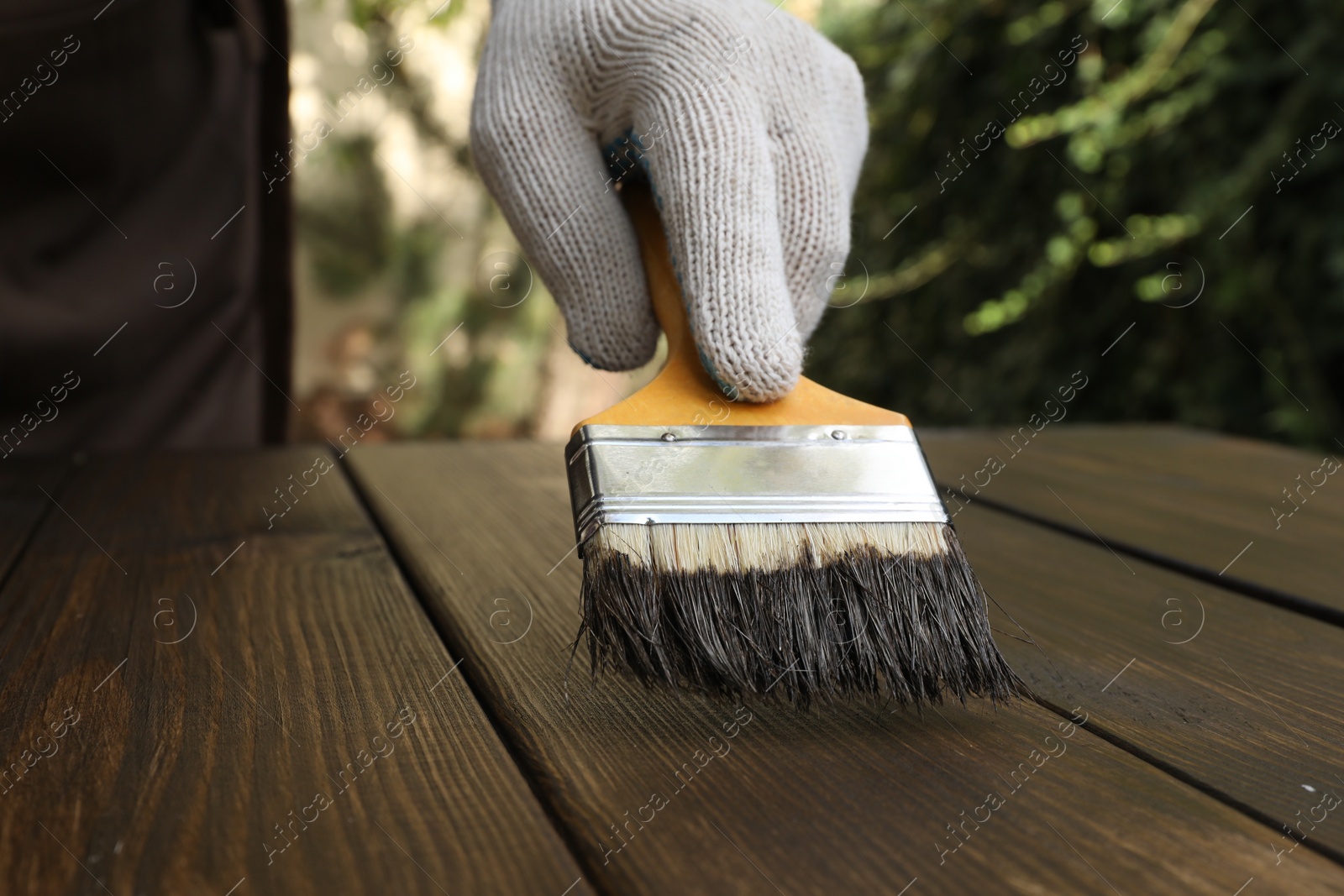 Photo of Man applying wood stain onto wooden surface outdoors, closeup