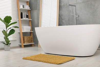 Stylish bathroom interior with soft yellow bath mat and tub