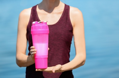 Athletic young woman with protein shake at riverside, closeup