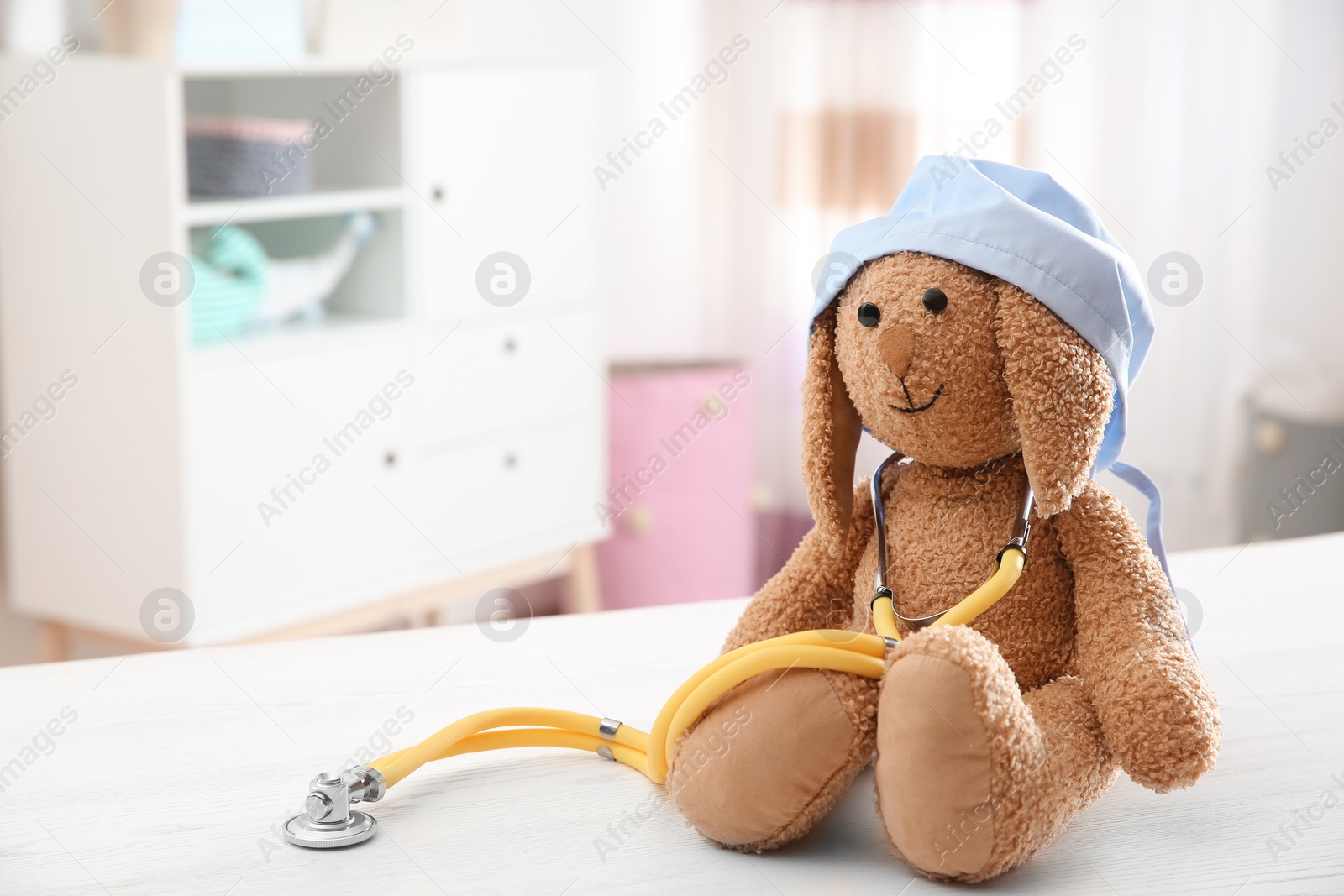 Photo of Toy bunny with medical cap and stethoscope on table indoors, space for text. Children's doctor
