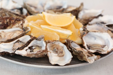 Photo of Fresh oysters with cut juicy lemon on plate, closeup