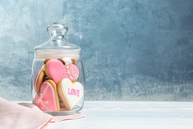 Photo of Decorated heart shaped cookies in glass jar on table. Space for text