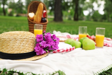 Photo of Straw hat, flowers and food for summer picnic on blanket outdoors