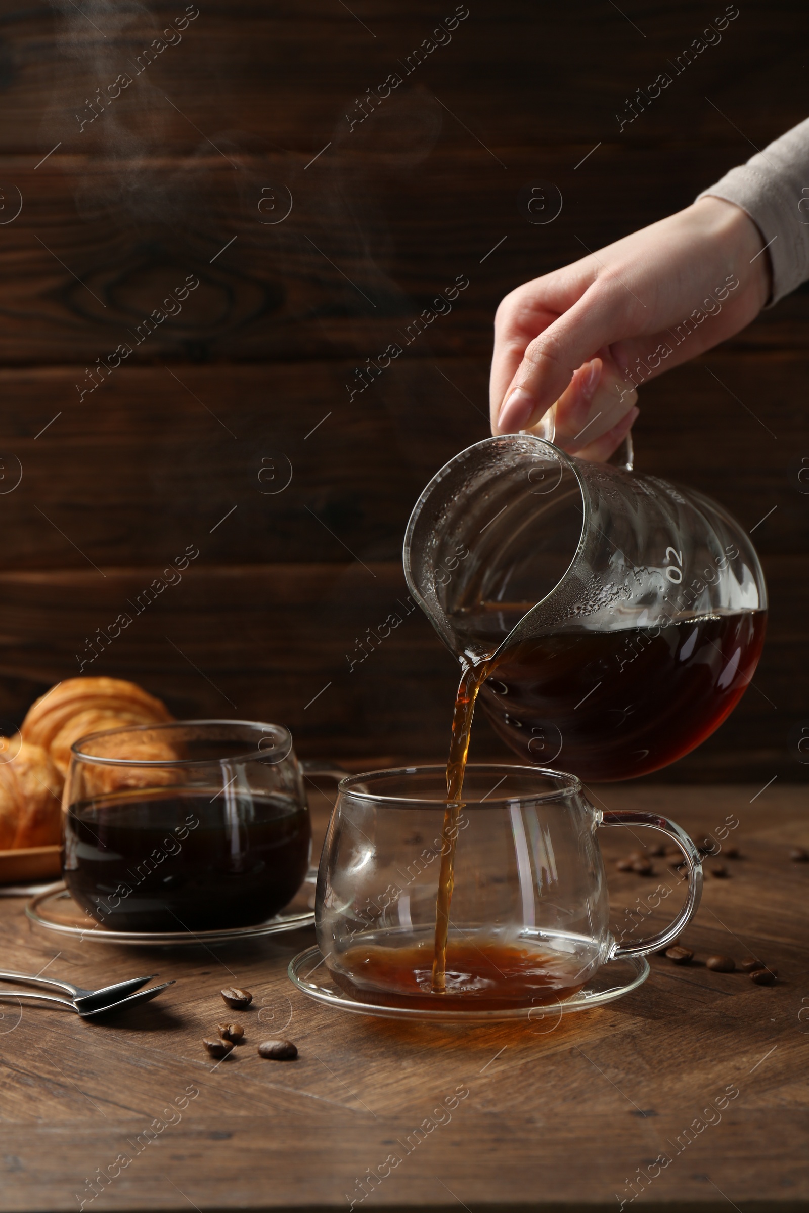 Photo of Woman pouring coffee into glass cup at wooden table, closeup