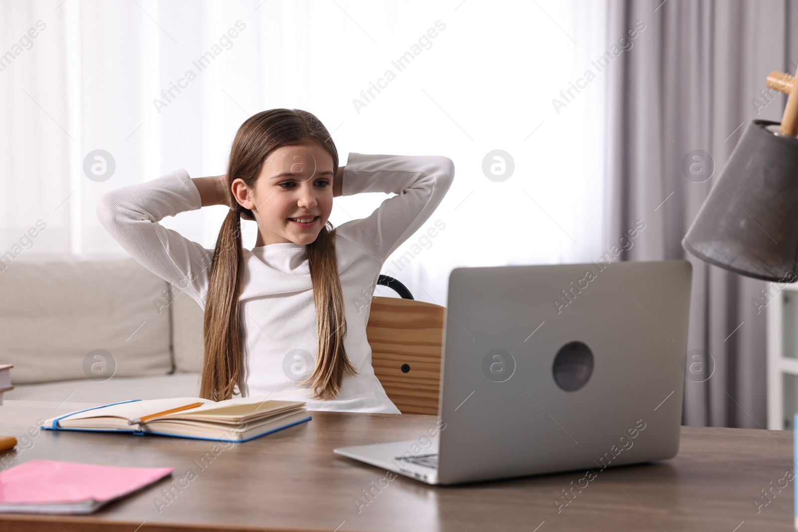 Photo of E-learning. Cute girl using laptop during online lesson at table indoors