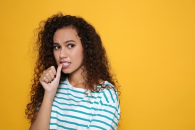 African-American woman biting her nails on yellow background. Space for text
