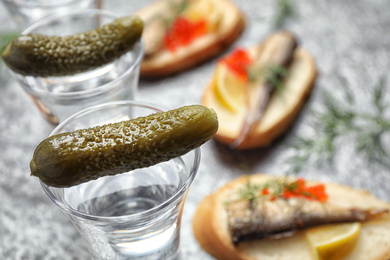 Photo of Cold Russian vodka with pickles on grey table, closeup
