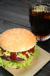 Burger with delicious patty and soda drink on black wooden table