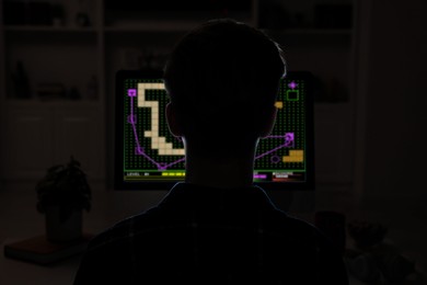 Image of Gaming disorder. Teenager playing on computer in darkness, back view