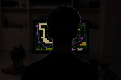 Gaming disorder. Teenager playing on computer in darkness, back view