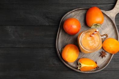 Photo of Tasty persimmon smoothie with straw and fresh fruits on black wooden table, top view. Space for text