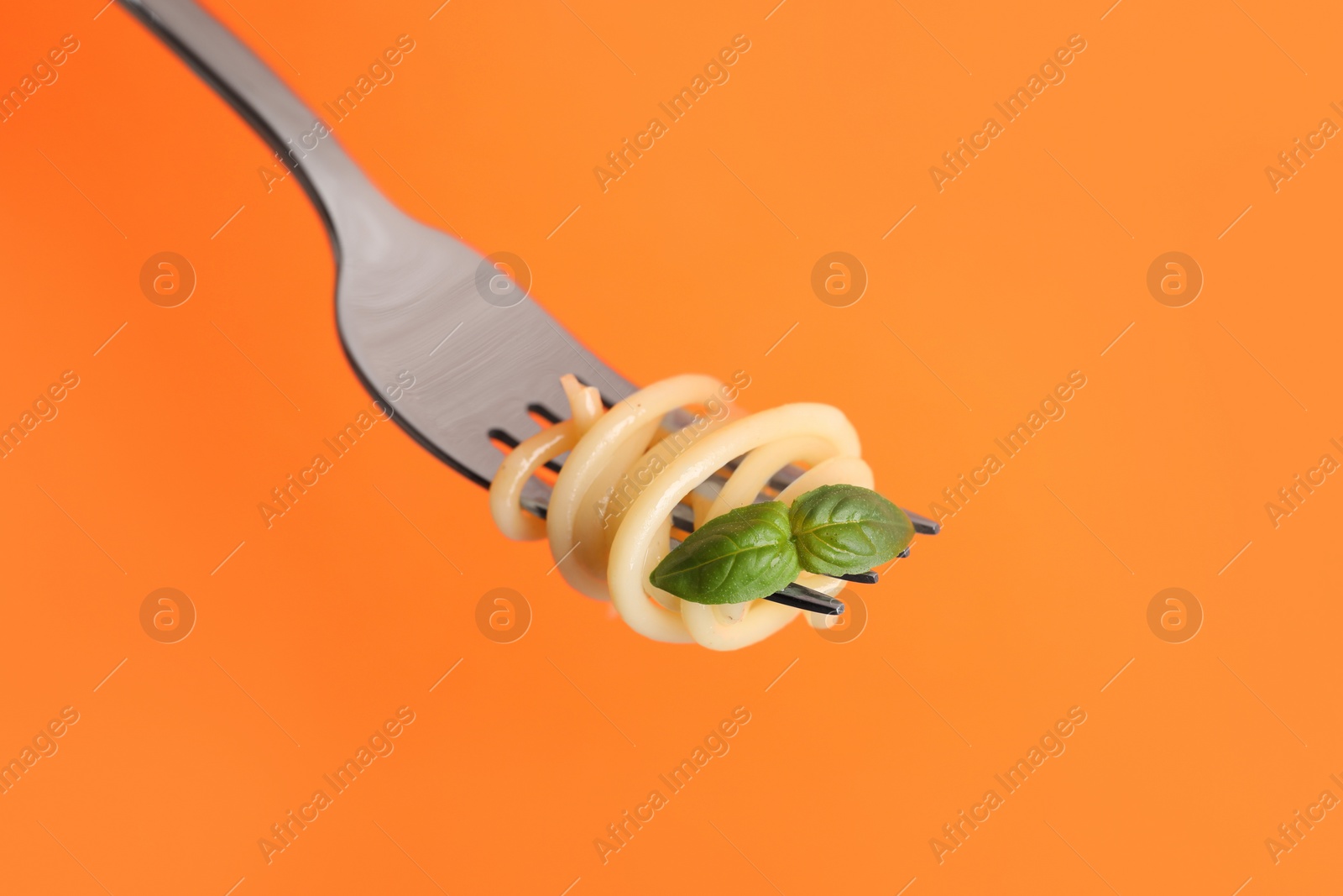 Photo of Fork with tasty pasta and basil on orange background, closeup