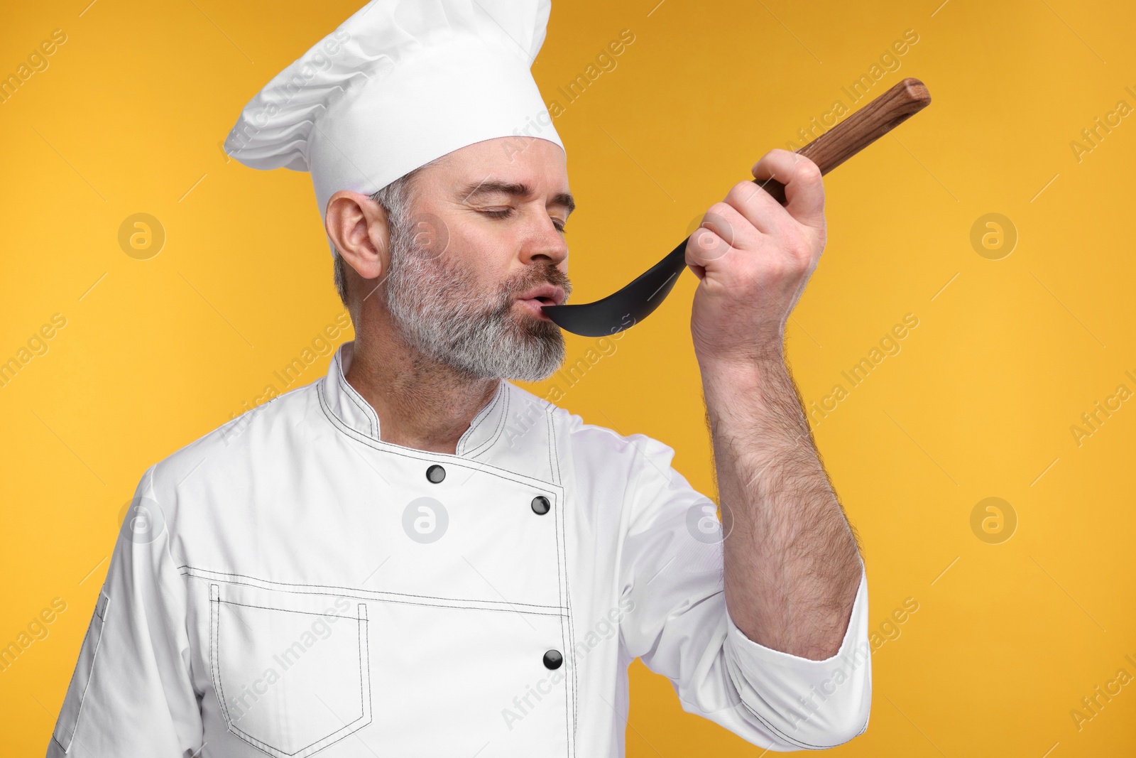 Photo of Chef in uniform tasting something on orange background