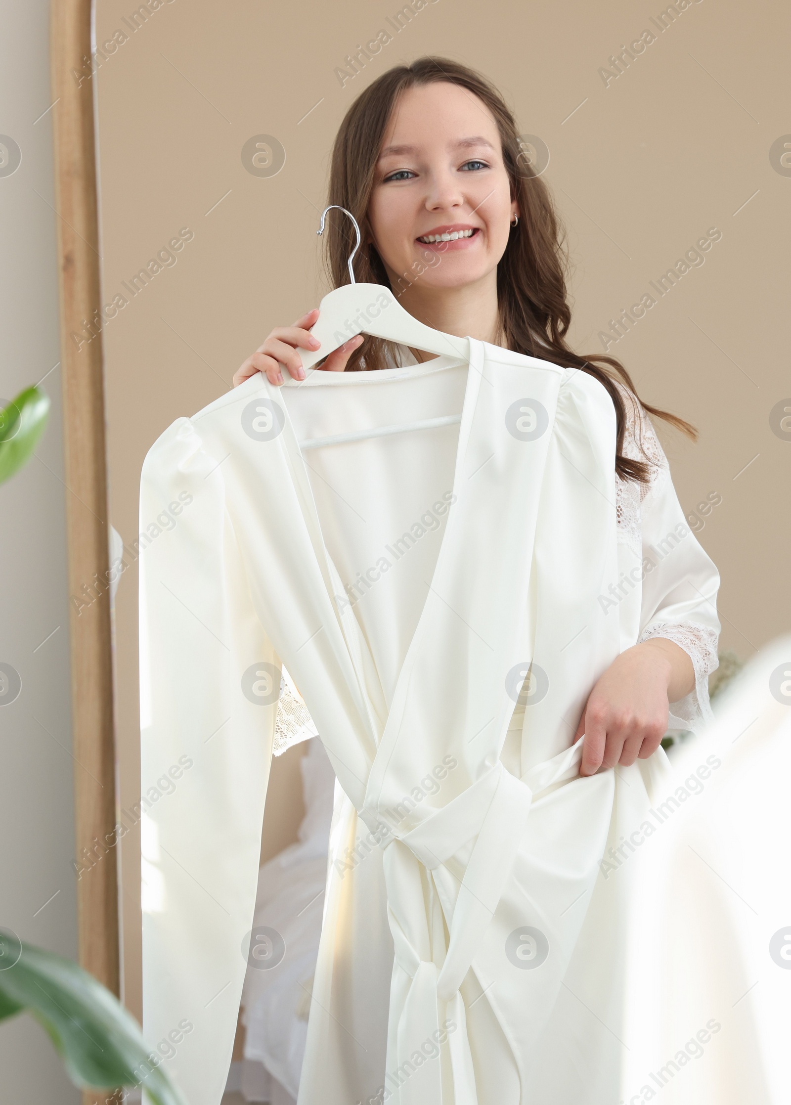 Photo of Happy young bride with her beautiful wedding dress near mirror at home