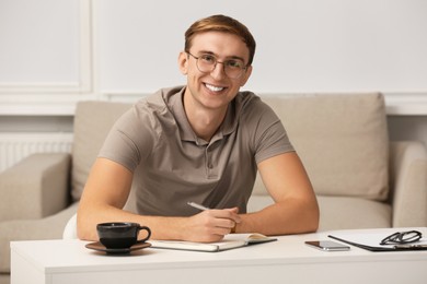 Young man writing in notebook at table indoors