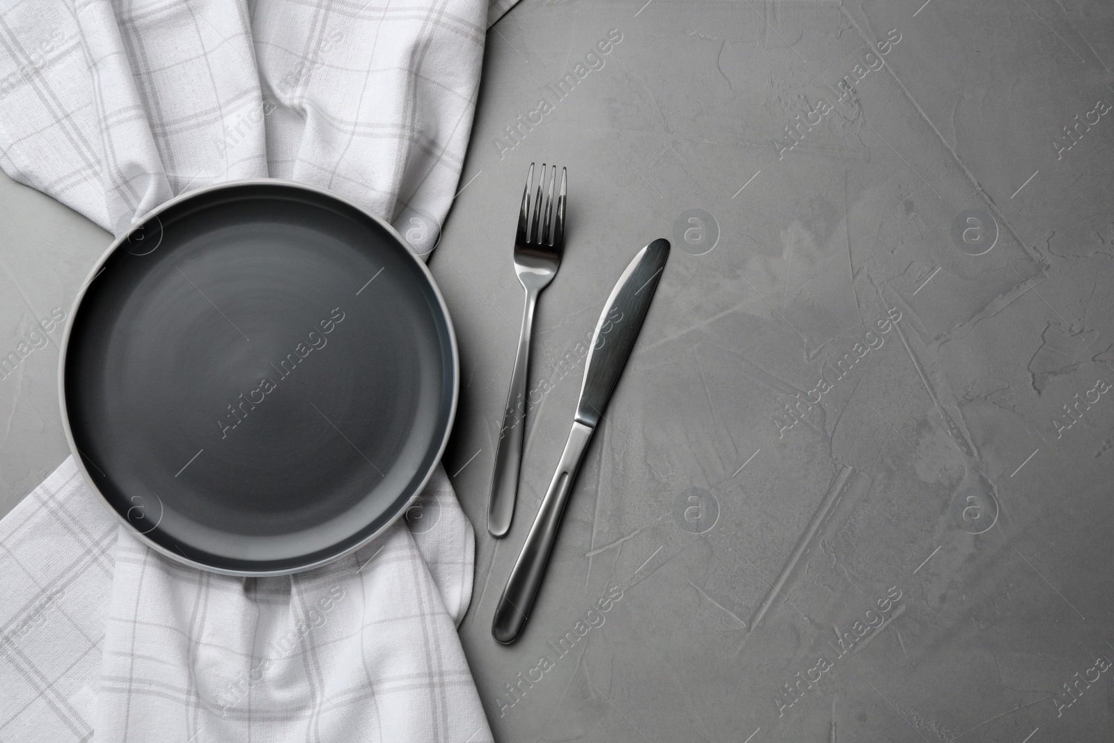 Photo of New dark plate, cutlery and napkin on grey table, flat lay. Space for text