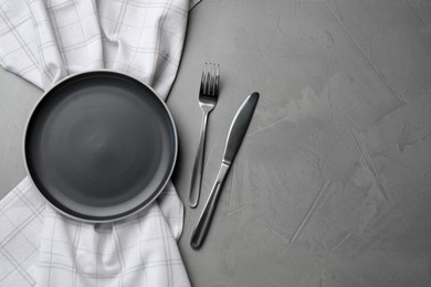 Photo of New dark plate, cutlery and napkin on grey table, flat lay. Space for text