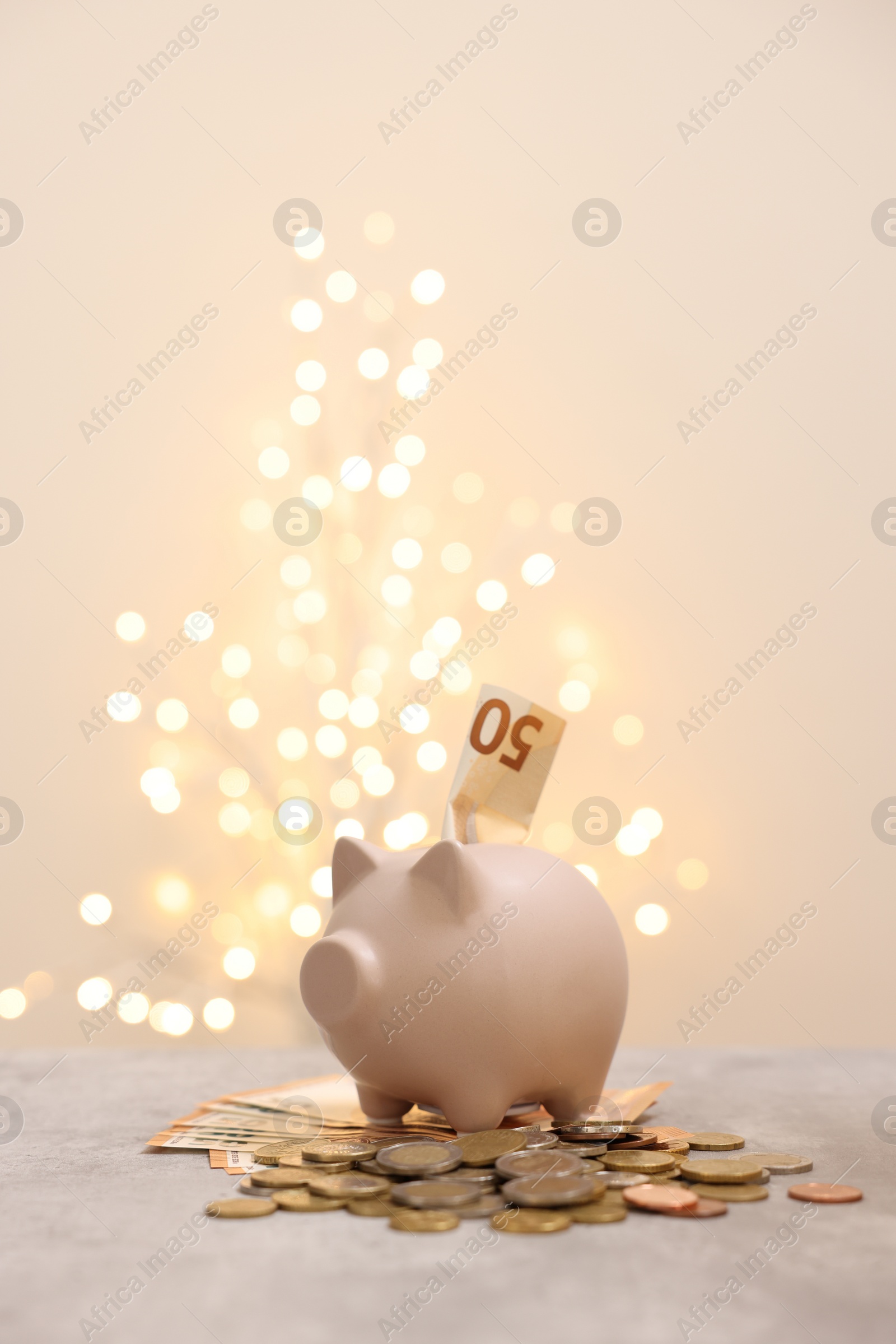 Photo of Piggy bank with euro banknote and coins on grey table against blurred lights, space for text