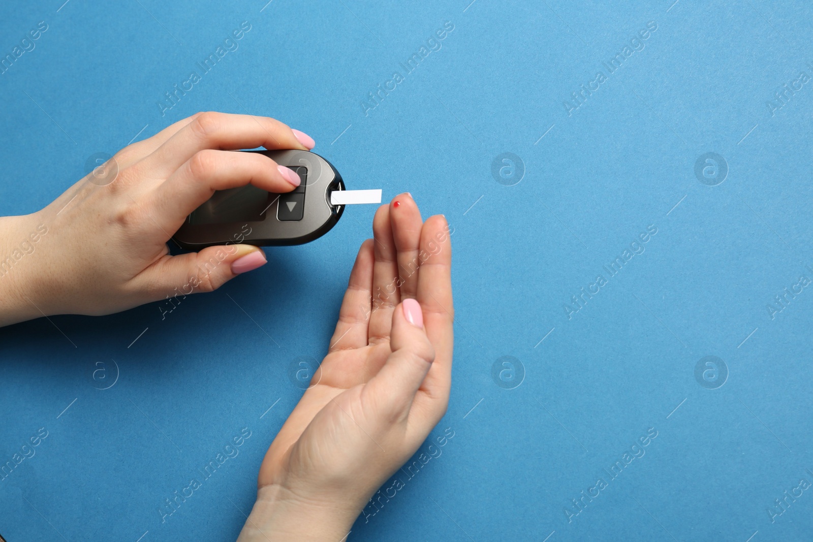 Photo of Diabetes. Woman checking blood sugar level with glucometer on light blue background, top view. Space for text