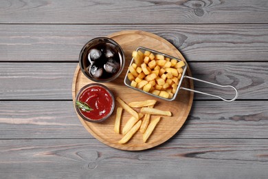 Photo of Tasty French fries, soda and ketchup on grey wooden table, top view