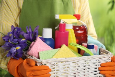 Woman holding basket with spring flowers and cleaning supplies outdoors, closeup