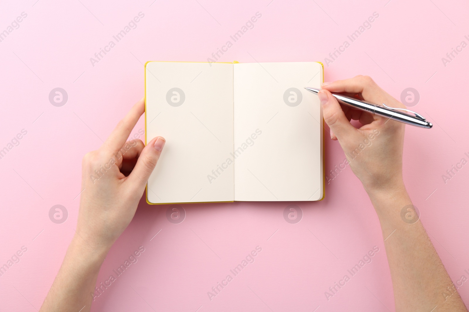 Photo of Woman writing in notebook on pink background, top view