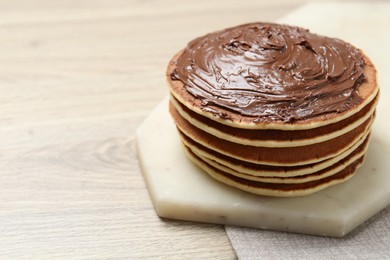 Photo of Delicious pancakes with chocolate paste on wooden table, closeup. Space for text